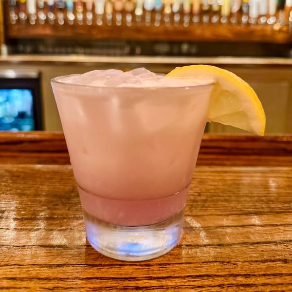 A pink cocktail with ice and a lemon wedge sits on a wooden bar at The Rickhouse.