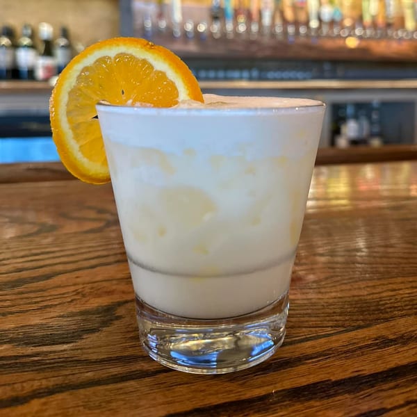 A creamy cocktail with an orange slice garnish sits on a wooden bar at The Rickhouse.