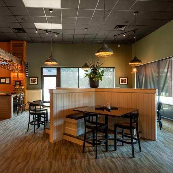 Restaurant interior with high-top tables, booths, a bar area, and industrial pendant lighting.
