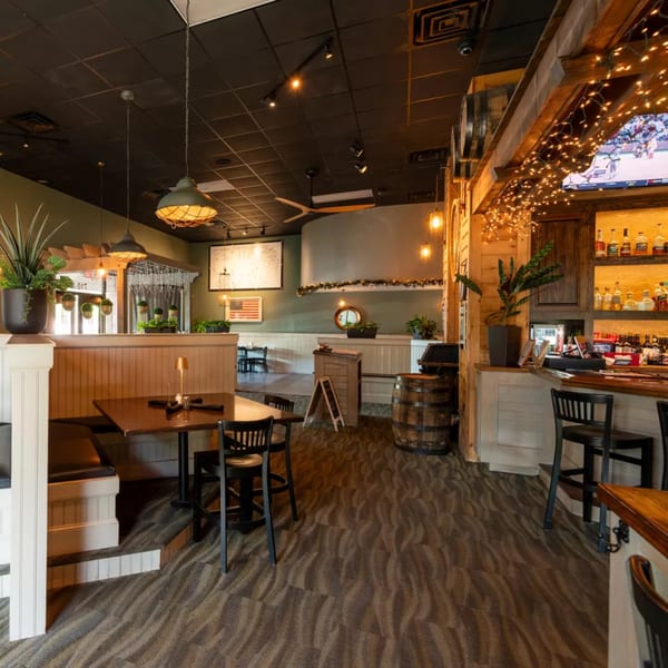 Cozy restaurant interior with booth seating, wooden tables, a bar, and warm lighting.