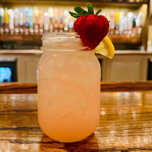 A refreshing strawberry lemonade in a mason jar with a lemon slice on a wooden bar.
