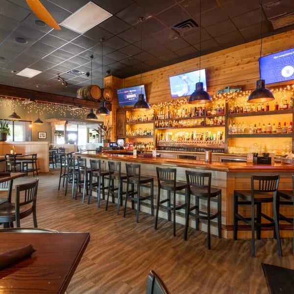 A rustic bar area with wooden walls, numerous liquor bottles, beer taps, and bar stools.